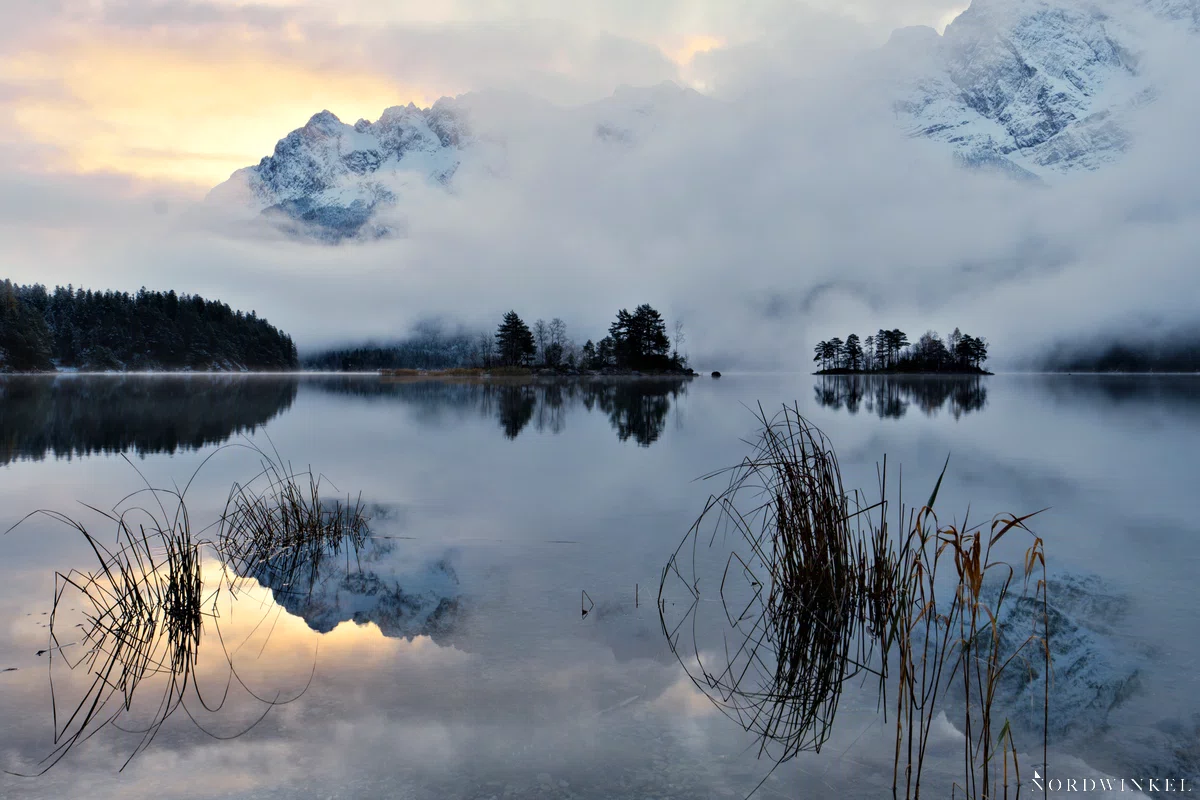 sonnenaufgang an gebirgssee mit felswand und nebelbank im hintergrund