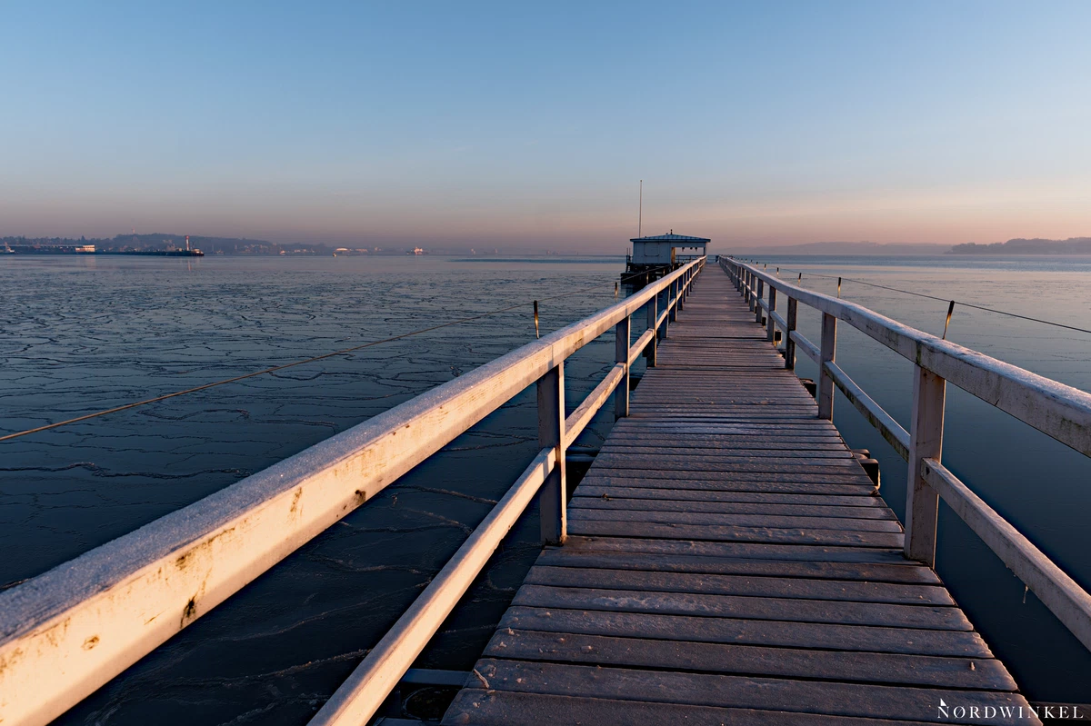 geländer mit steg führen bei wolkenlosem sonnenaufgang über die gefrorene ostsee zu einer hütte,