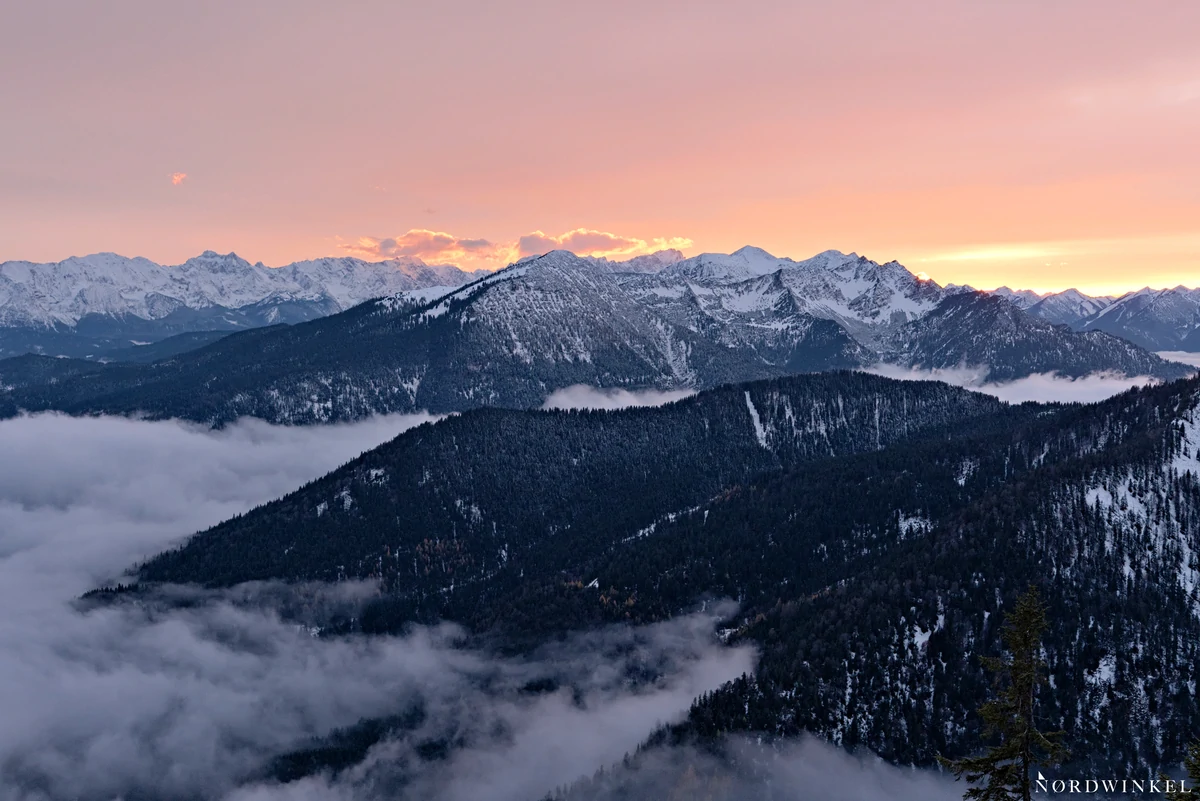 schneebedeckte berggipfel zum sonnenuntergang und darunter liegenden wolkenschichten