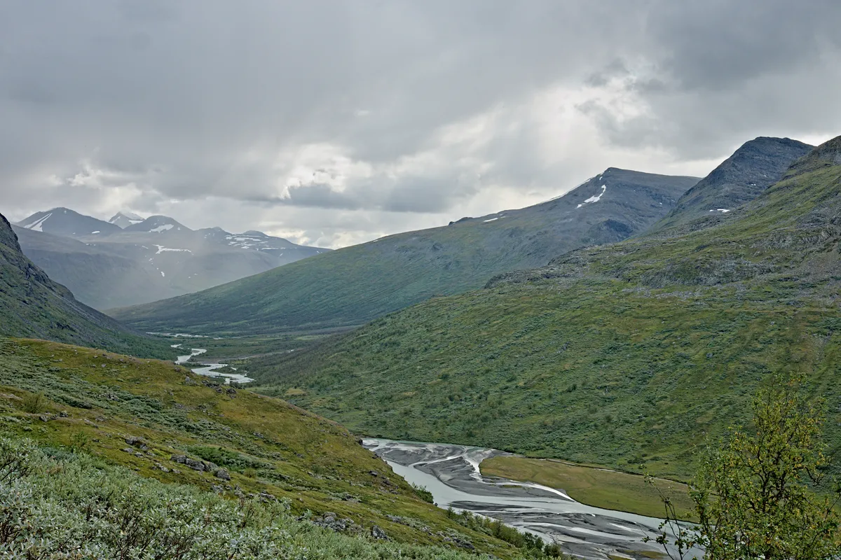 blick bei schlechtem wetter über ein grünes flusstal in den bergen