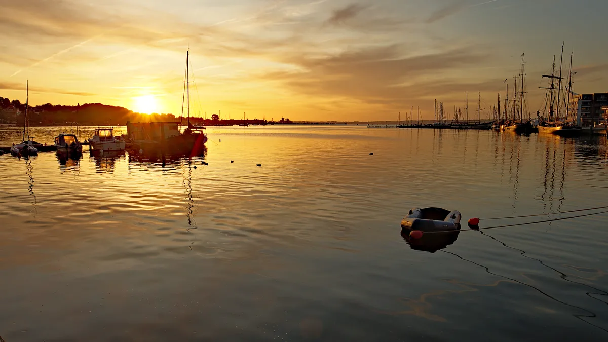 hafenansicht mit kleinen booten und größeren segelschiffen zum sonnenaufgang