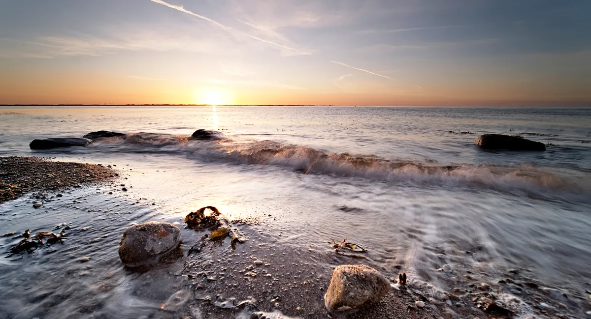 brechende welle mit steinen am ostseestrand zum sonnenuntergang